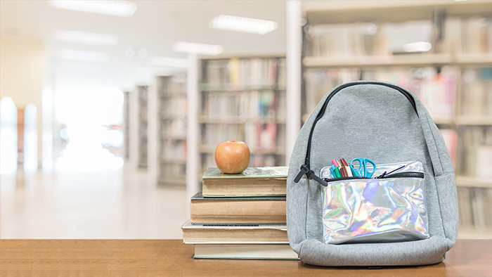 Stack of books with an apple on top, beside a backpack. 