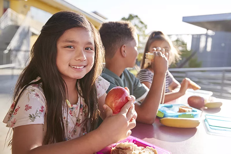 Kids sitting at a table eating health food.