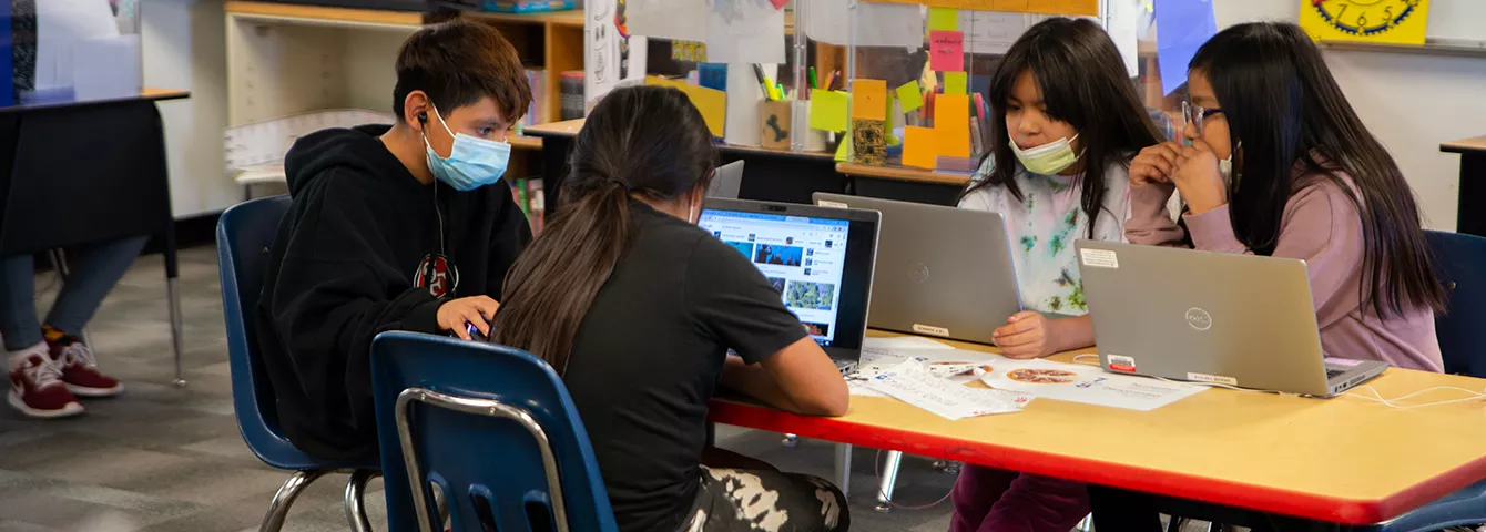 Students at a table working on their laptops in class.