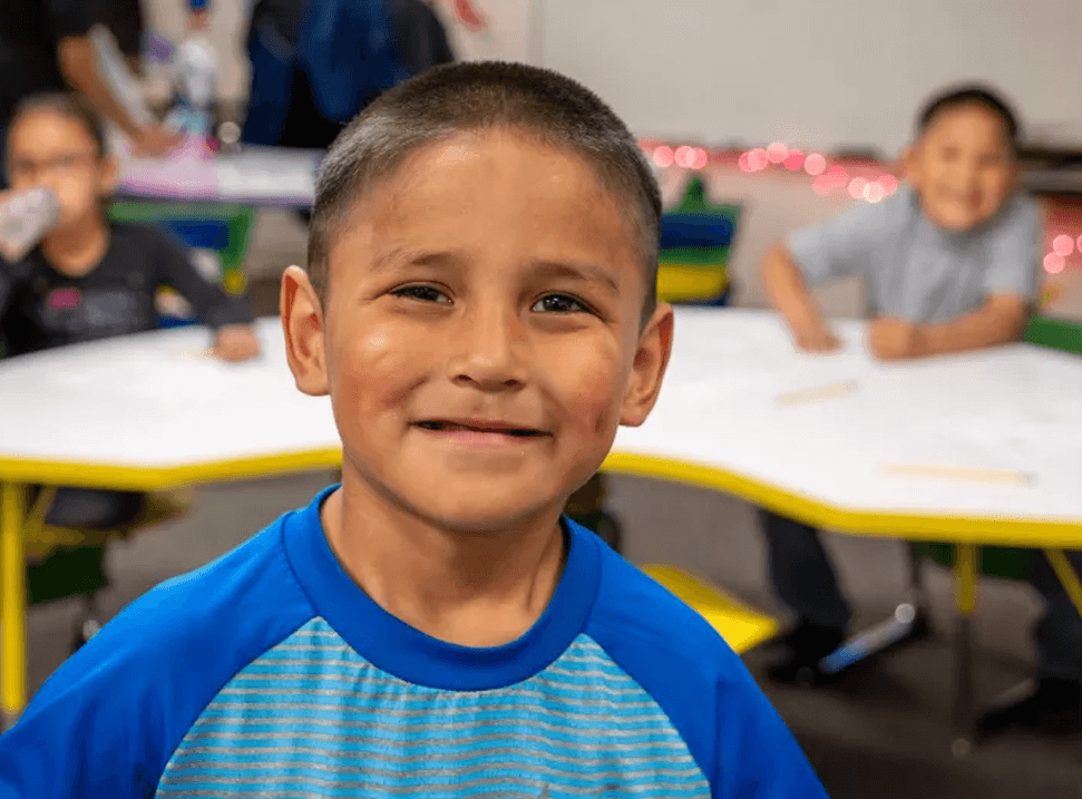 Young boy smiling at the camera in a classroom.