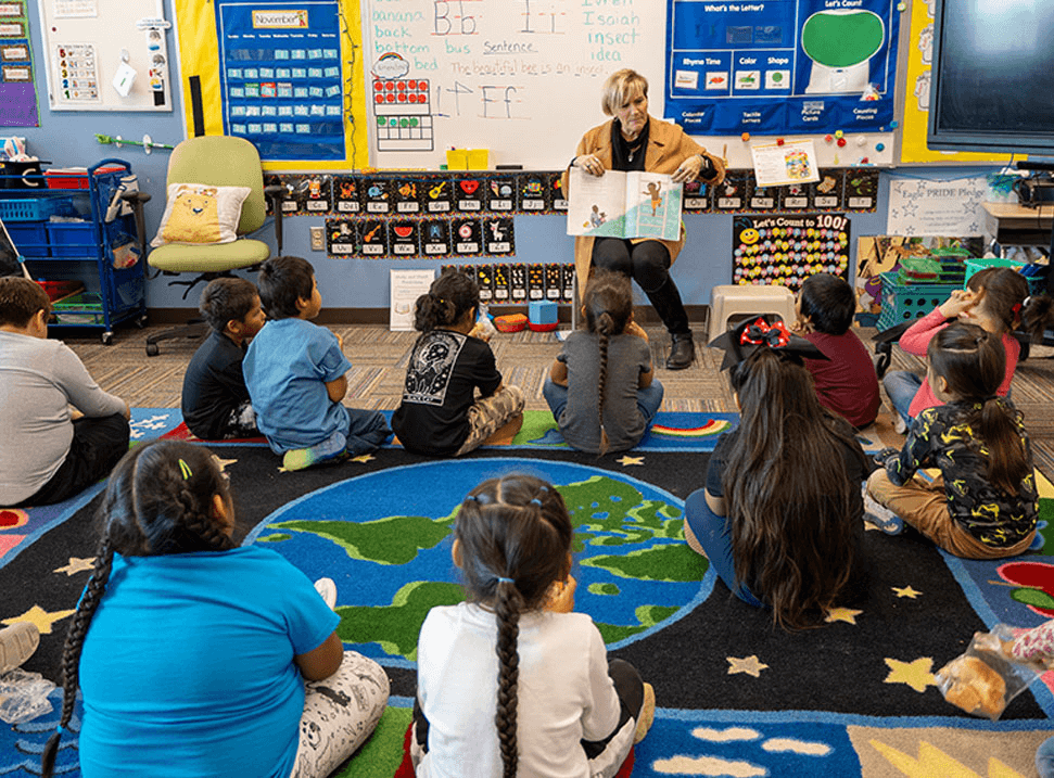 Teacher reading to a classroom of students who are sitting on the floor. 