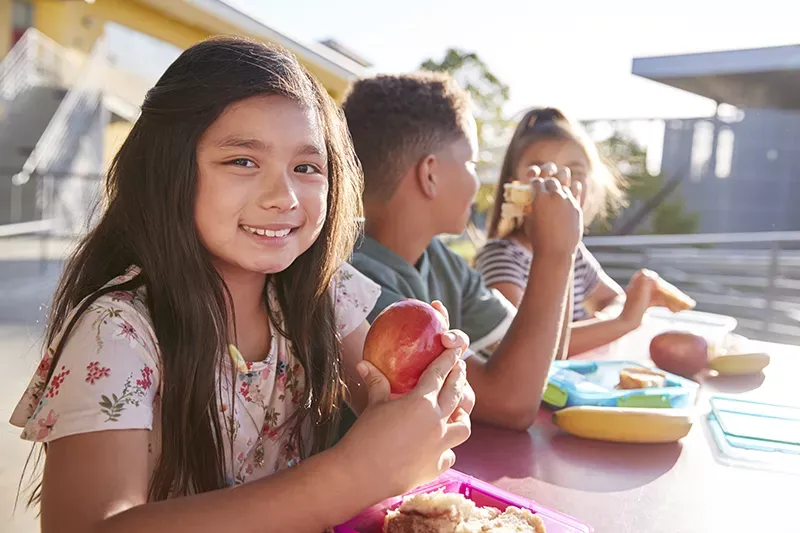 Kids sitting at a table eating health food.